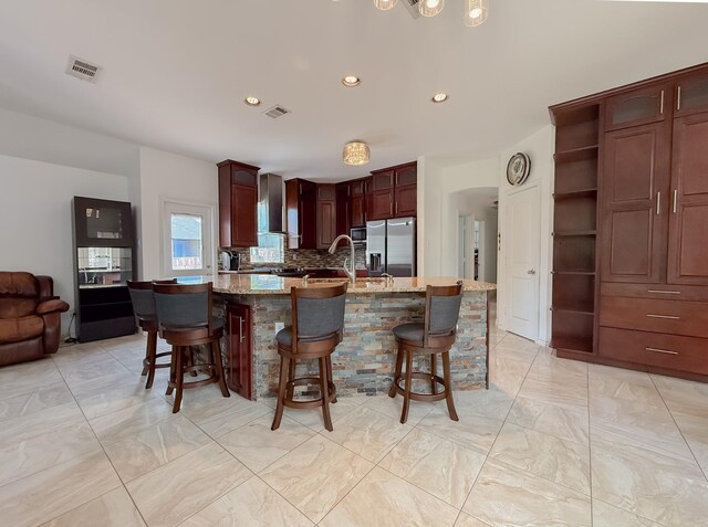 kitchen featuring backsplash, visible vents, appliances with stainless steel finishes, marble finish floor, and wall chimney exhaust hood