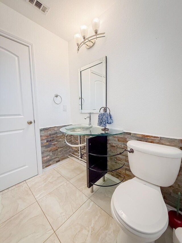 bathroom with a notable chandelier, a sink, toilet, a wainscoted wall, and visible vents