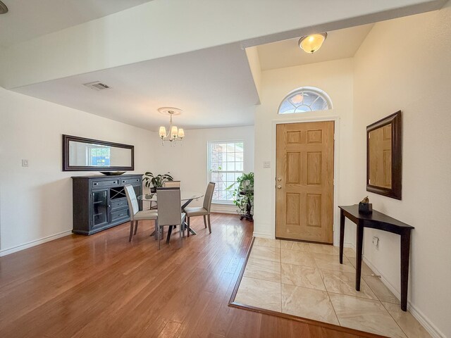 foyer entrance with an inviting chandelier, baseboards, light wood-style floors, and visible vents