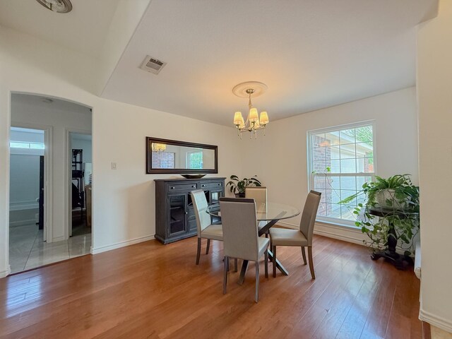 dining room featuring arched walkways, a notable chandelier, visible vents, and wood finished floors