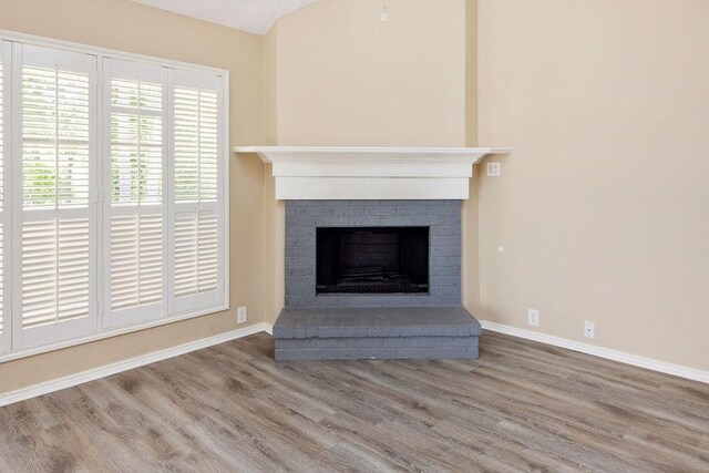 room details featuring baseboards, a brick fireplace, and wood finished floors