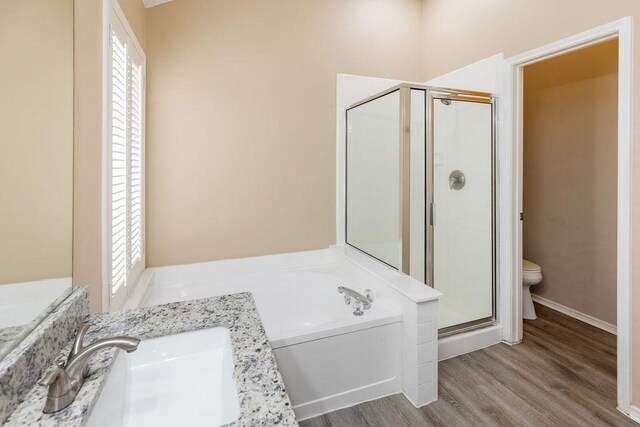 bathroom with vanity, toilet, wood finished floors, a bath, and a stall shower
