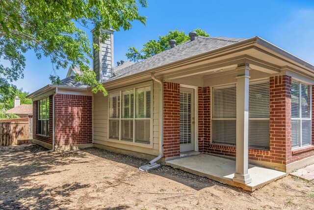 back of house with a chimney, roof with shingles, a patio area, brick siding, and fence