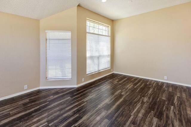 empty room with dark wood-type flooring, a textured ceiling, baseboards, and vaulted ceiling