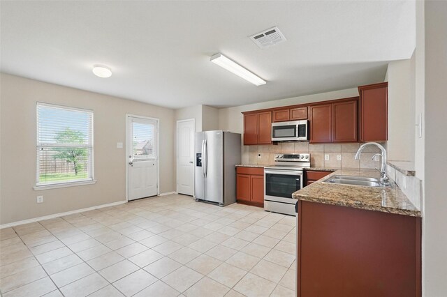 kitchen with visible vents, tasteful backsplash, light stone countertops, a sink, and stainless steel appliances
