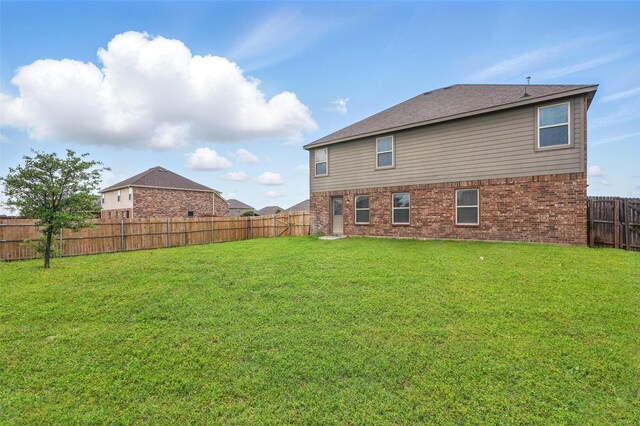 rear view of property featuring brick siding, a fenced backyard, and a yard