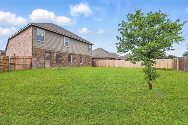 back of property featuring a yard, brick siding, and a fenced backyard