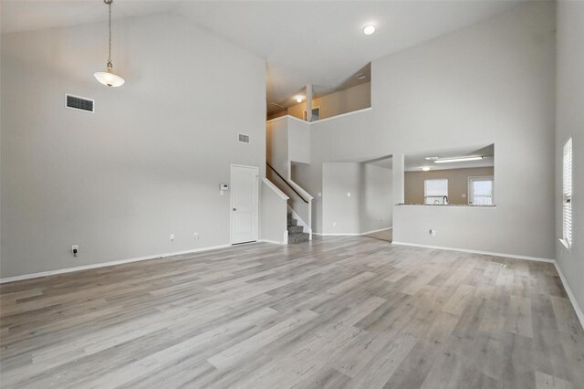 unfurnished living room with visible vents, stairway, high vaulted ceiling, baseboards, and light wood-style flooring