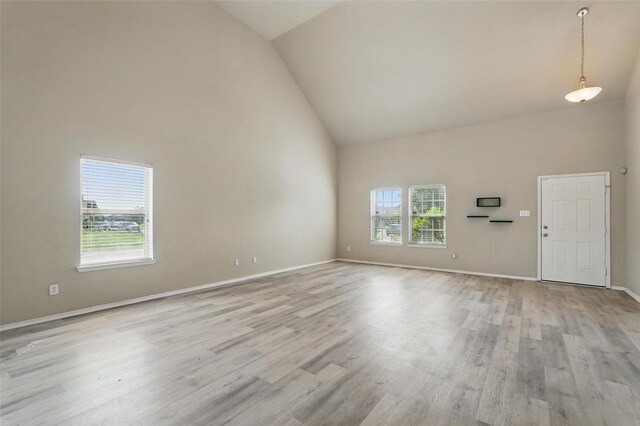 unfurnished living room featuring baseboards, light wood-style flooring, a wealth of natural light, and high vaulted ceiling