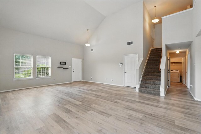 unfurnished living room with light wood-style floors, high vaulted ceiling, stairs, washer / dryer, and visible vents