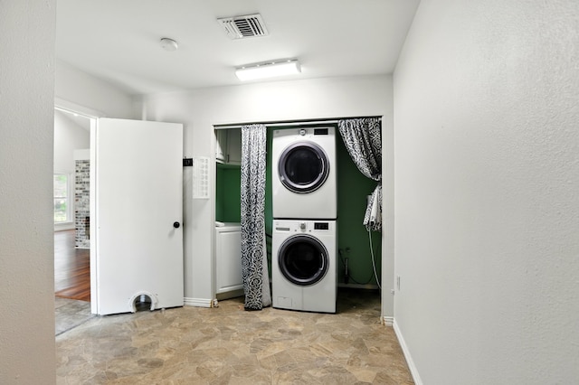 laundry area featuring laundry area, visible vents, baseboards, stone finish flooring, and stacked washer / drying machine