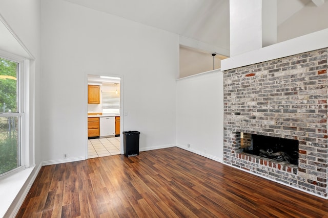 unfurnished living room with high vaulted ceiling, baseboards, a brick fireplace, and wood finished floors