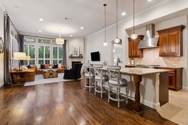 2206 Glasgow Dr, Trophy Club, TX 76262 - kitchen featuring wall chimney exhaust hood, ornamental molding, light stone counters, open floor plan, and brown cabinetry