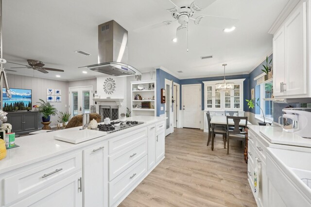 kitchen featuring visible vents, ceiling fan with notable chandelier, white cabinetry, and island range hood