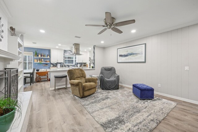 living room with light wood-type flooring, a ceiling fan, recessed lighting, and ornamental molding