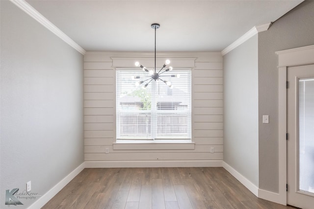 unfurnished dining area featuring an inviting chandelier, ornamental molding, and wood finished floors
