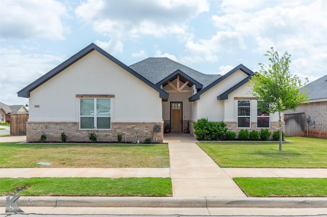 view of front of property with a front lawn, fence, stucco siding, brick siding, and a shingled roof