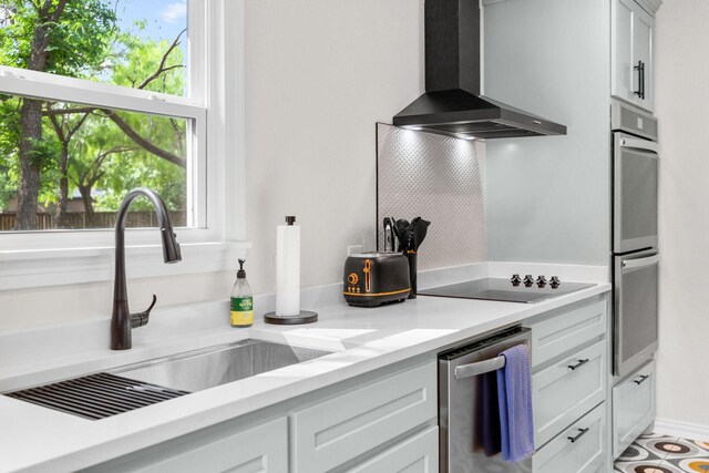 kitchen with light countertops, a sink, wall chimney exhaust hood, and stainless steel appliances