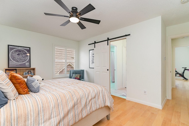 bedroom with light wood-style floors, baseboards, a ceiling fan, and a barn door