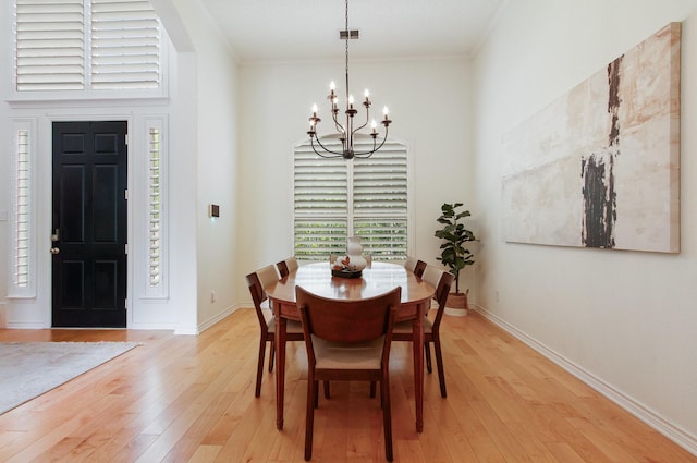 dining space featuring crown molding, an inviting chandelier, a towering ceiling, and light wood-style floors