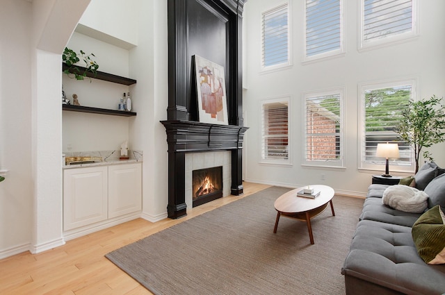 living room with a high ceiling, light wood-style floors, baseboards, a tile fireplace, and indoor bar