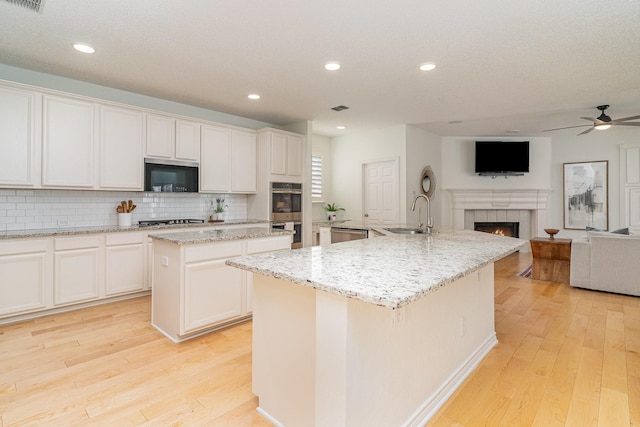 kitchen featuring a sink, appliances with stainless steel finishes, light wood-type flooring, and an island with sink