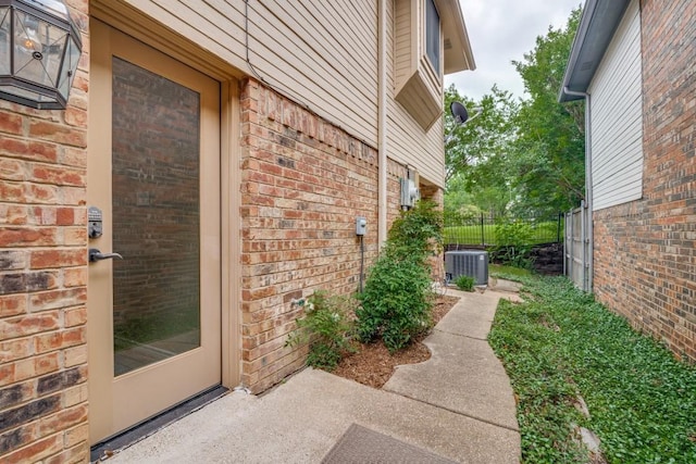 view of property exterior featuring fence, cooling unit, and brick siding