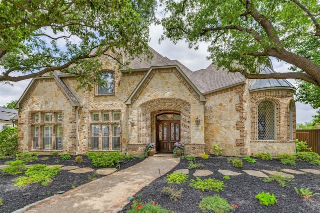 view of front of home featuring french doors, brick siding, fence, a shingled roof, and stone siding