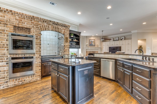 kitchen featuring appliances with stainless steel finishes, a sink, a fireplace, a kitchen island, and visible vents