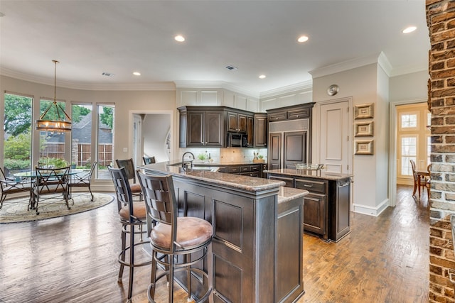 kitchen with dark brown cabinetry, dark wood-style flooring, black microwave, a center island, and a sink