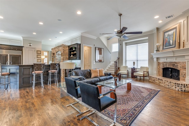 living area with ceiling fan, crown molding, a fireplace, wood finished floors, and stairs