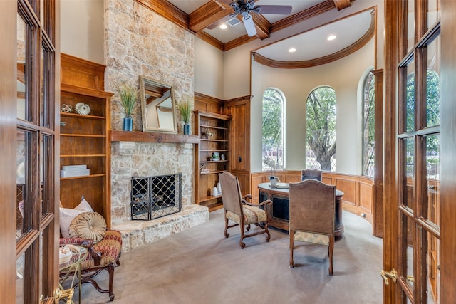 carpeted dining room featuring crown molding, a stone fireplace, a wainscoted wall, a ceiling fan, and recessed lighting