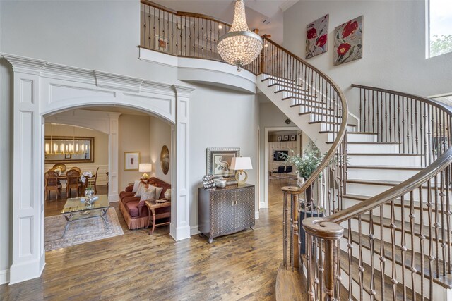 entryway featuring an inviting chandelier, wood finished floors, a high ceiling, stairway, and arched walkways