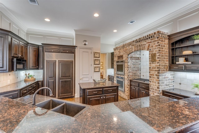kitchen with dark brown cabinets, black microwave, a sink, paneled refrigerator, and visible vents