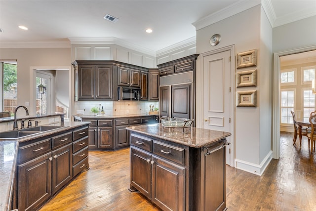 kitchen with dark brown cabinetry, visible vents, black microwave, a center island, and paneled fridge
