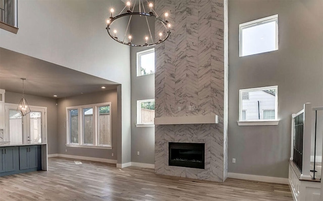 unfurnished living room with baseboards, light wood finished floors, a towering ceiling, and a notable chandelier