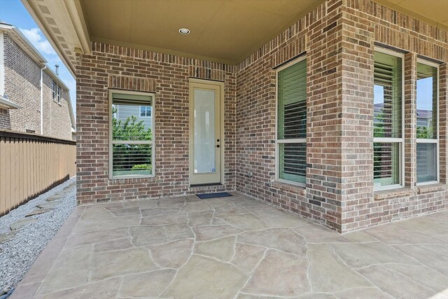 property entrance featuring brick siding, fence, and a patio