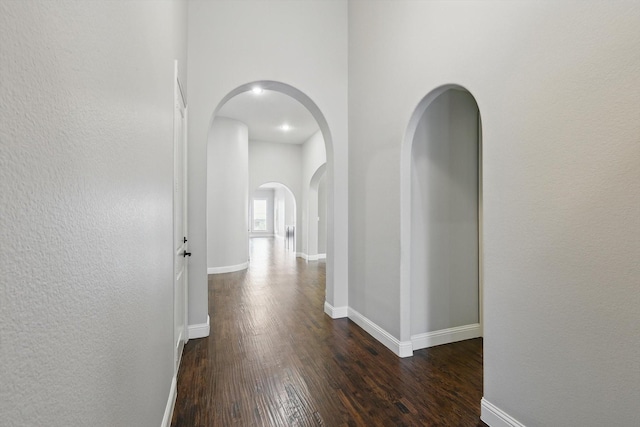 corridor with baseboards, arched walkways, and wood finished floors