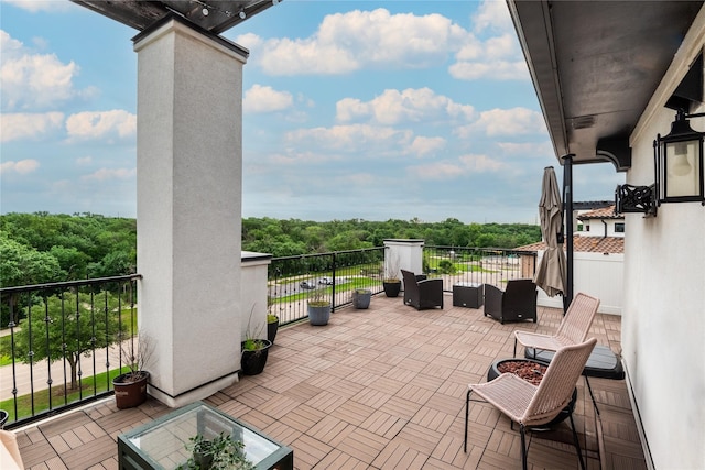 view of patio with a forest view, an outdoor living space, and a balcony