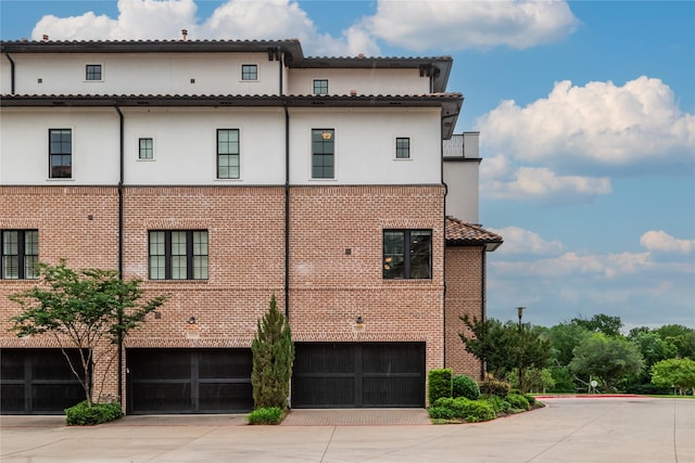 view of side of home featuring a garage, stucco siding, concrete driveway, and brick siding
