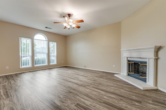 unfurnished living room with a fireplace with raised hearth, a ceiling fan, baseboards, wood finished floors, and visible vents
