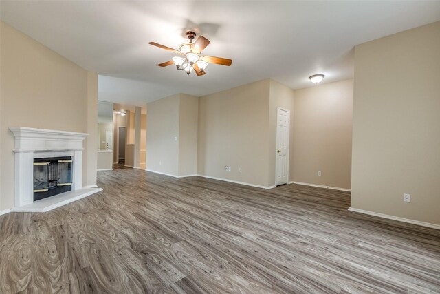 unfurnished living room with baseboards, ceiling fan, a glass covered fireplace, and wood finished floors