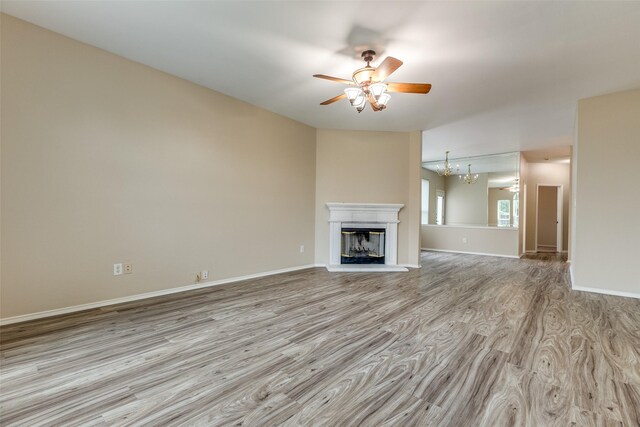 unfurnished living room with baseboards, a glass covered fireplace, wood finished floors, and ceiling fan with notable chandelier