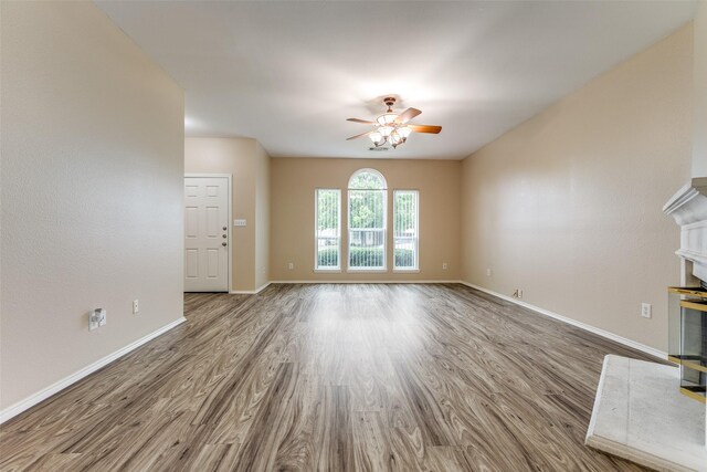 unfurnished living room featuring baseboards, a ceiling fan, wood finished floors, and a fireplace