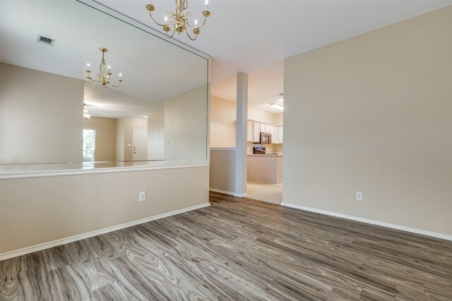 spare room with baseboards, visible vents, wood finished floors, and a notable chandelier