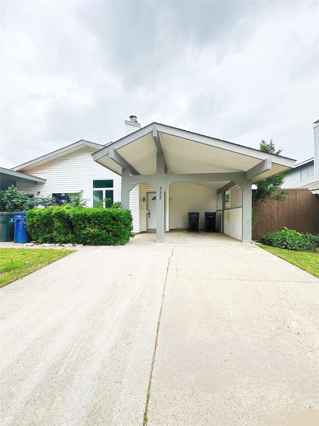 view of front of home featuring fence, a chimney, driveway, and an attached carport