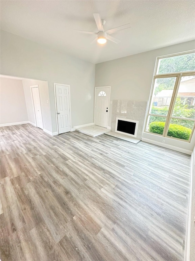 unfurnished living room featuring ceiling fan, baseboards, light wood-style floors, and a fireplace