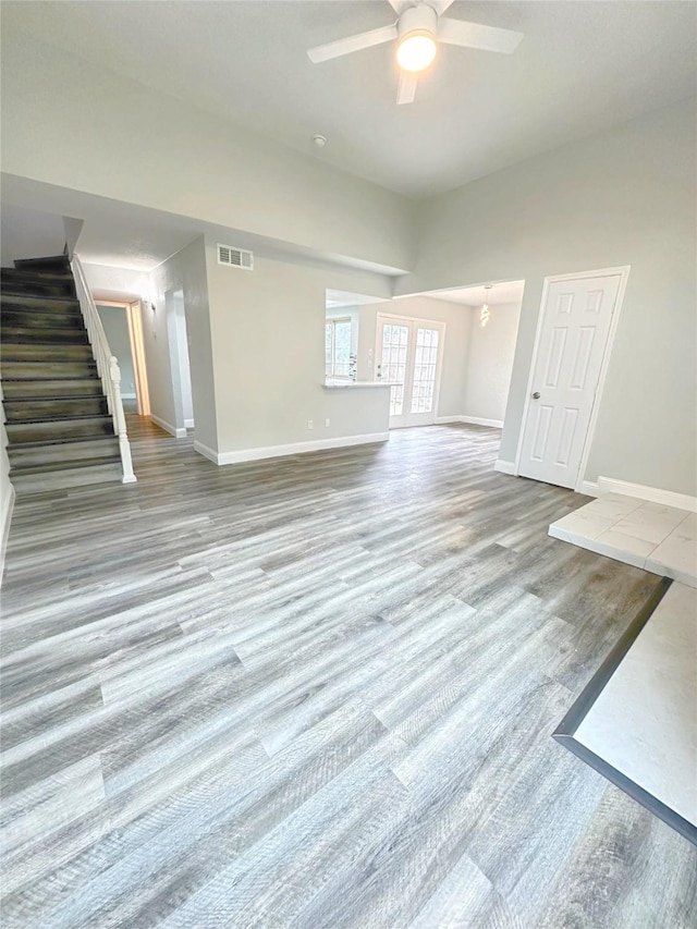 unfurnished living room with ceiling fan, visible vents, wood finished floors, baseboards, and stairs