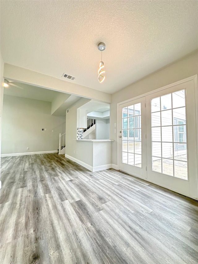 unfurnished living room featuring baseboards, visible vents, a textured ceiling, and wood finished floors