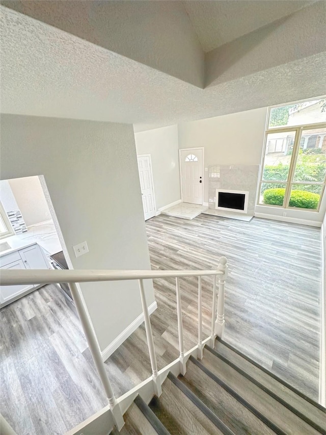 staircase featuring wood finished floors, baseboards, a high end fireplace, a textured ceiling, and vaulted ceiling